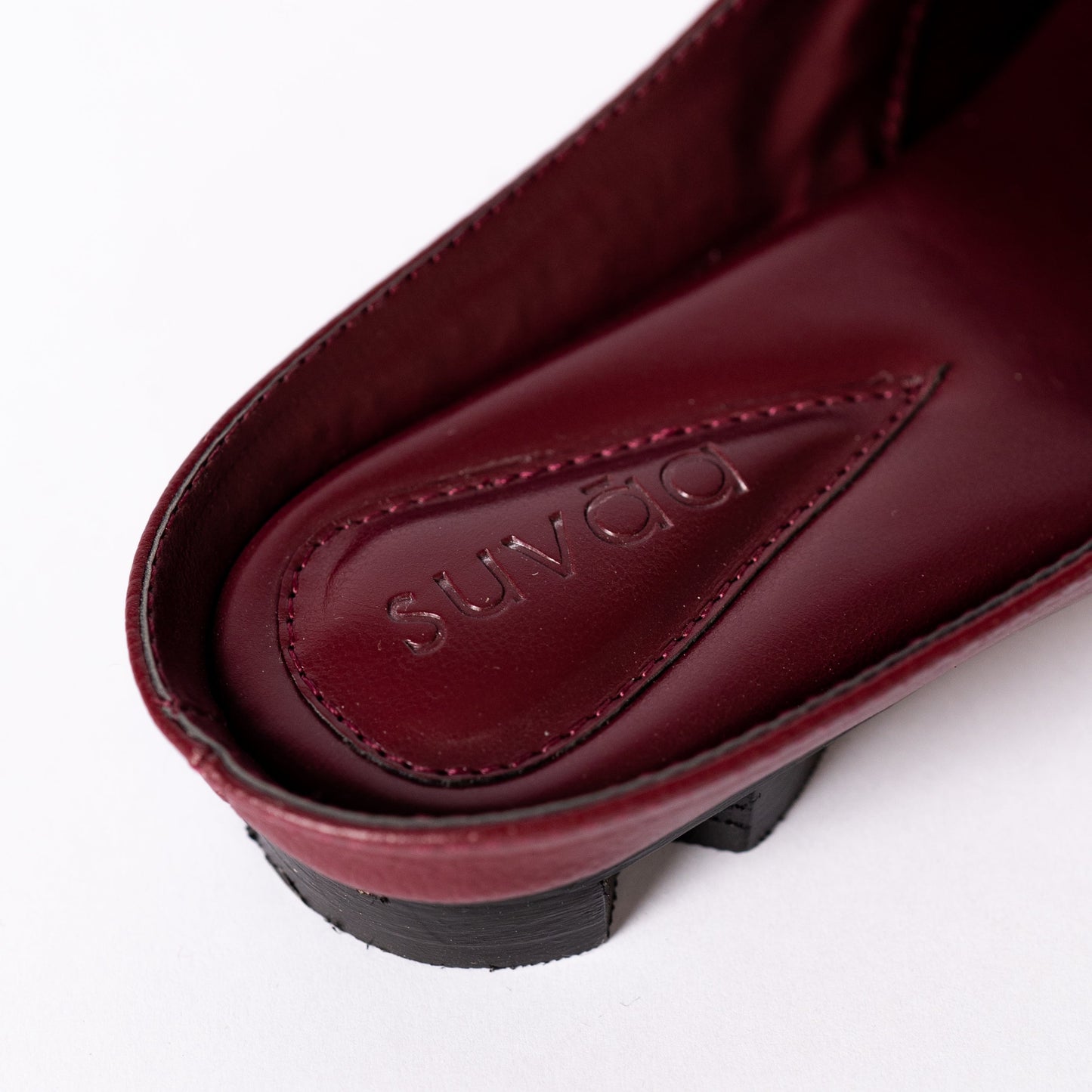 Close-up of a maroon shoe with 'Suvāa' branding on a white background.
