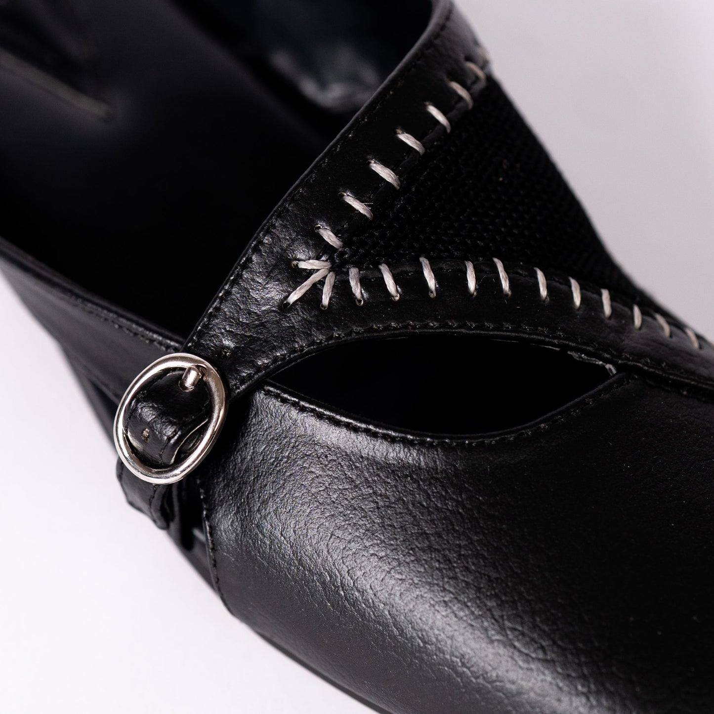 Close-up of a black mule with a decorative buckle on a white background.